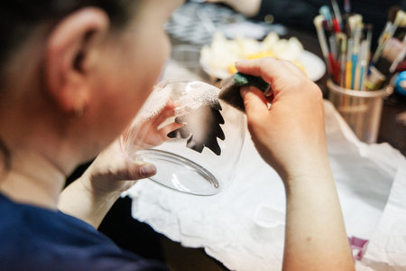 In a Christmas Craft workshop, a person is creating intricate designs on a glass using a tool, surrounded by various art supplies and materials.の写真素材
