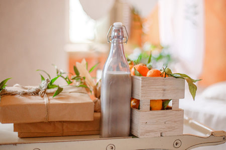 A tray sits on a bed, holding a glass bottle filled with milk, a wooden crate filled with oranges, and a wrapped gift box.の写真素材