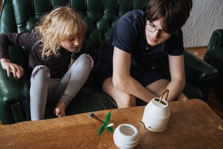 Siblings engaged in creative play at home with objects on a wooden table in natural light during the afternoonの写真素材