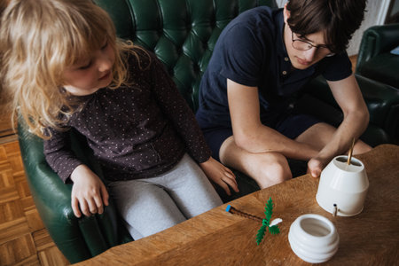 A child and an adult sit together on a green couch, focusing on a creative project at a wooden table, enjoying quality time on a relaxing afternoon.の写真素材