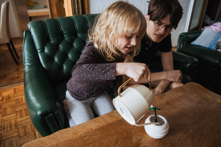Smiling girl carefully pouring water into a small plant pot with her older brother watching, learning and caring for plants.の写真素材