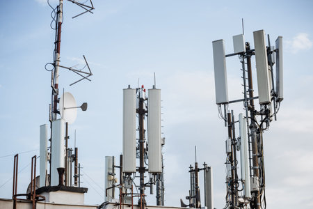 Multiple telecommunication antennas installed on a rooftop against a clear blue sky. Modern...