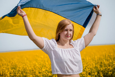 A middle-aged woman connects with nature and nationhood while holding the Ukrainian flag in a bright yellow field.の写真素材