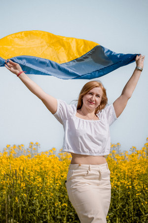 A cheerful and symbolic portrait of a woman with Ukraine s flag in a rapeseed field during Independence Day.の写真素材