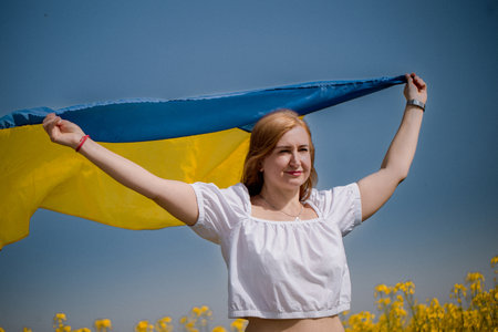 Middle-aged woman holding the national flag beside a blooming rapeseed field during National Flag Dayの写真素材
