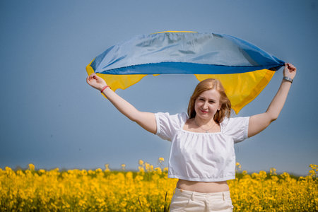 Symbolic gesture of national pride as a woman waves the flag of Ukraine near a flowering rapeseed field on Constitution Dayの写真素材