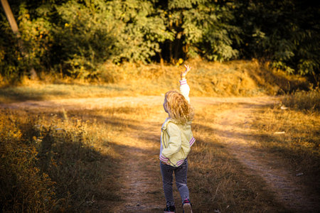 Child joyfully running along a dirt path in warm afternoon sunlight with vibrant greenery surroundingの写真素材