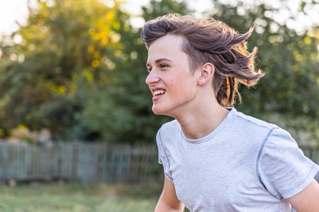 A young man with flowing hair runs joyfully in a park under the warm sunlight. The vibrant greenery creates a lively backdrop for this energetic outdoor activity.の写真素材