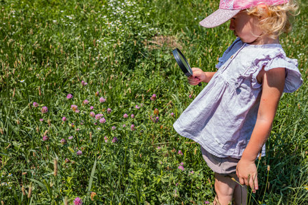 A young girl studies red clover flower heads in a meadow using a hand lens playful outdoor botany and STEM learning.の写真素材