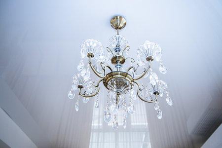 A beautiful chandelier with crystal accents hangs from the ceiling, casting a warm glow in a bright, contemporary space. Its intricate design adds charm and elegance to the room.の写真素材