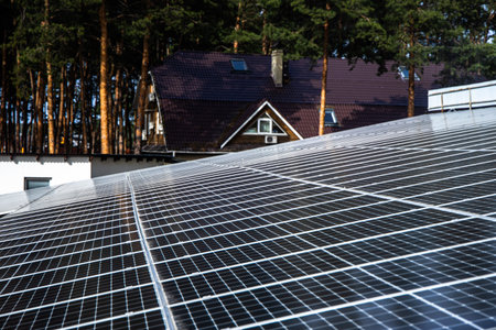 Solar panels are installed on a roof in a quiet forest area. Sunlight reflects off the panels, showing renewable energy being utilized near homes surrounded by trees.の写真素材