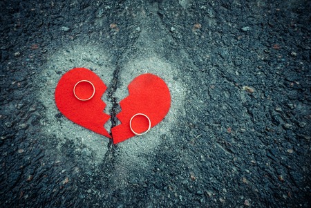 Divorce concept - broken red heart with wedding rings on cracked asphalt. Tonedの写真素材