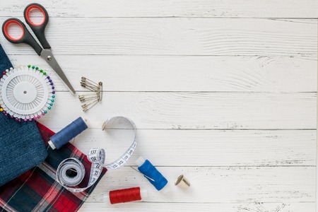 Sewing accessories, denim and plaid fabric on a white wooden background. Fabric, sewing threads, needle, pins, scissors, buttons and sewing centimeter. Copyspaceの写真素材