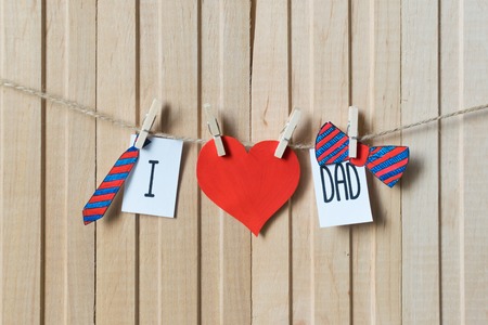 Fathers day concept. Message with paper hearts, tie and bow-tie hanging with pins over light wooden board.の写真素材