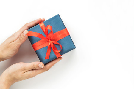 Blue Gift box with red ribbon in womans hands on white background. Top view. Copyspaceの写真素材