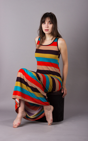 Young Girl in Stretch Dress on Grey Background Sitting on Stoolの写真素材