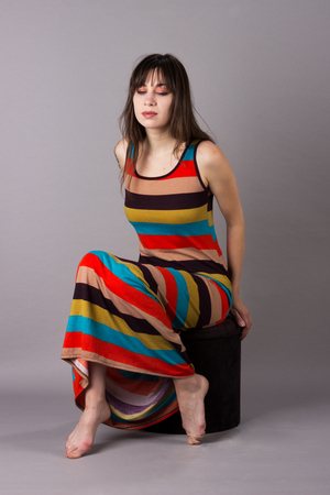Young Girl in Stretch Dress on Grey Background Sitting on Velvet Stoolの写真素材
