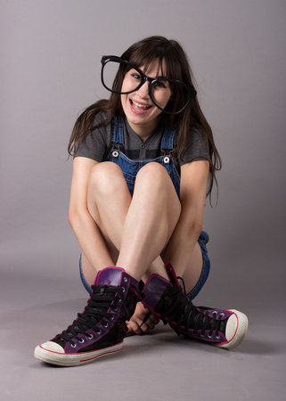 Sitting Cute Young Millennial Woman in Overalls and Cute Shoesの写真素材