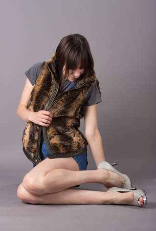 Cute Young Millennial Woman in Furry Vest Sitting in Overalls and High Heel Shoesの写真素材