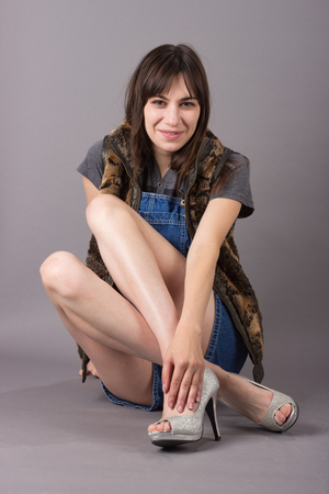 Smiling Cute Young Millennial Woman in Furry Vest Sitting in Overalls and High Heel Shoesの写真素材