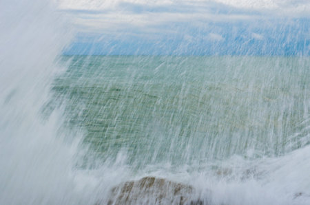splashing sea water over the rock with sea and sky in the background