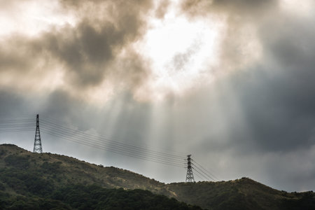 sun light beam through rain cloud over high voltage electrical wire and mountain
