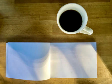 White empty page of paper with hot black coffee in cup on wood surface with early morning sunlight brighten up the dayの写真素材