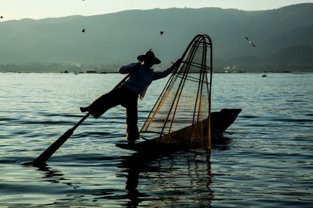 Inle Lake, Myanmar - circa Nov 2013: Burmese man rowing a small boat in Inle Lake. The Inle natives are famous for their unique leg rowing technique.のeditorial素材