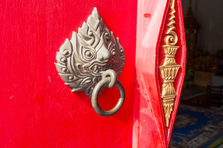 The ancient thai styles door handle or door knocker made from brass on red door.の写真素材