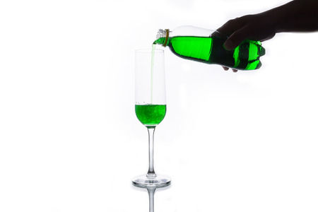 Green soda is poured from a  bottle into a glass, isolated on white.の写真素材