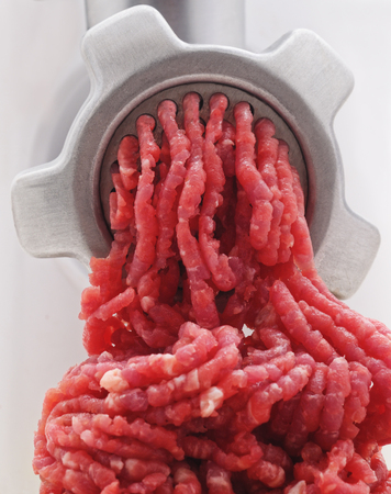 Process of meat grinding in the kitchen with mincing machine on a white background.の写真素材