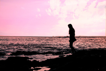 The woman standing on the rocks behind the sunset was a beautiful moment.の写真素材