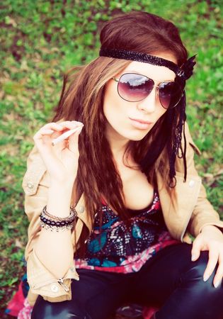 Beautiful young hippie girl sitting in the grass with cigaretteの写真素材