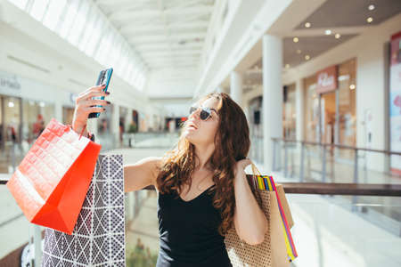 Young beautiful woman, shopping in a supermarket, holding colored bags with goods. and rejoices at the purchases madeの写真素材