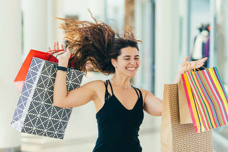 Young beautiful woman, shopping in a supermarket, holding colored bags with goods. and rejoices at the purchases madeの写真素材