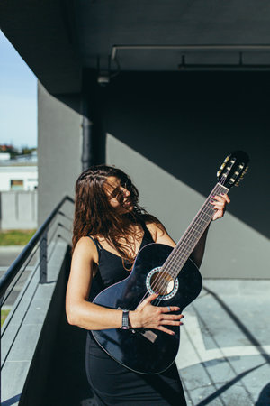 Beautiful woman with a black guitar in a dress in the car parkの写真素材