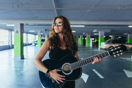 Beautiful woman with a black guitar in a dress in the car parkの写真素材