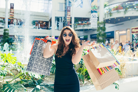 Young beautiful woman, shopping in a supermarket, holding colored bags with goods. and rejoices at...