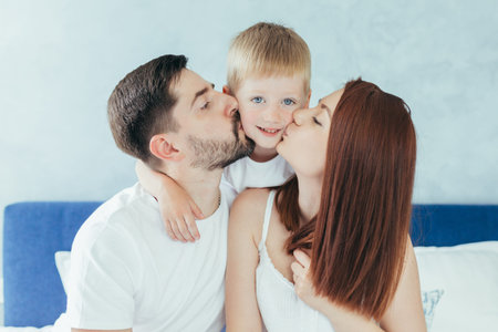 Young family woman, husband and son having fun together in a large bedroom in the morningの写真素材