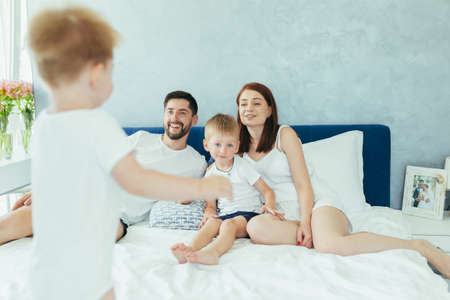 Young family husband wife and two young children, sons, have fun together in their bedroomの写真素材