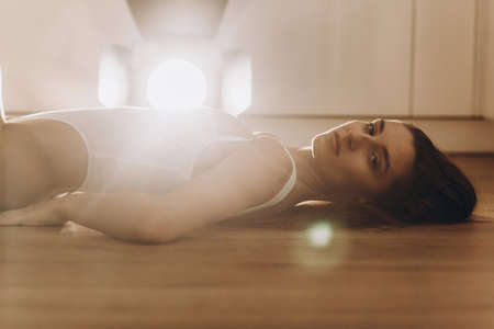 A young beautiful model woman is standing, posing in the kitchen in, white underwear. The girl has long dark hair, full lips and a beautiful face. Tanned, athletic, skinny body in the bodysuit.の写真素材