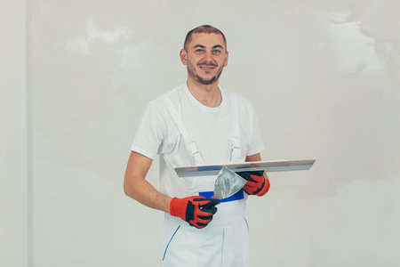 A man worker plasters the wall with a spatula and applies a cement mix solution. The repairman lays...