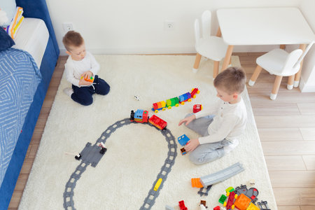 Two little brothers have fun in their nursery, play constructor and trainの写真素材