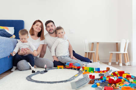 Young family, mom and dad with two young sons, playing with toys in the nursery, happy family having fun togetherの写真素材