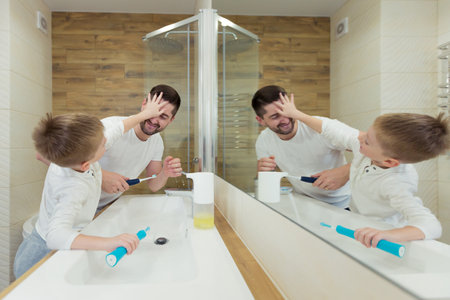 Father and young son brush their teeth in the morning, have fun togetherの写真素材