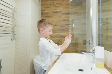 little blond boy washes his hands in the bathroom in the morning