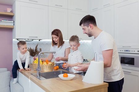 Young happy family with two young sons preparing breakfast together in their kitchen