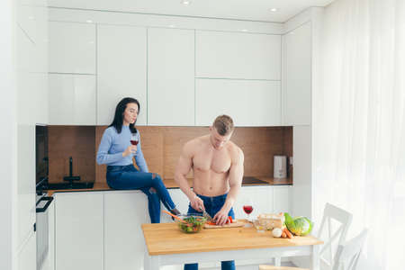 Athlete husband prepares lunch from vegetables to his wife, spend free time together in the kitchenの写真素材