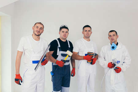 A team of construction workers, four people, men performing construction and repair work looking into the cameraの写真素材