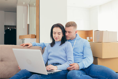 A couple in love with the newlyweds, moved to a new apartment, and use a laptop to choose new furniture for the apartment. make joint purchases online togetherの写真素材